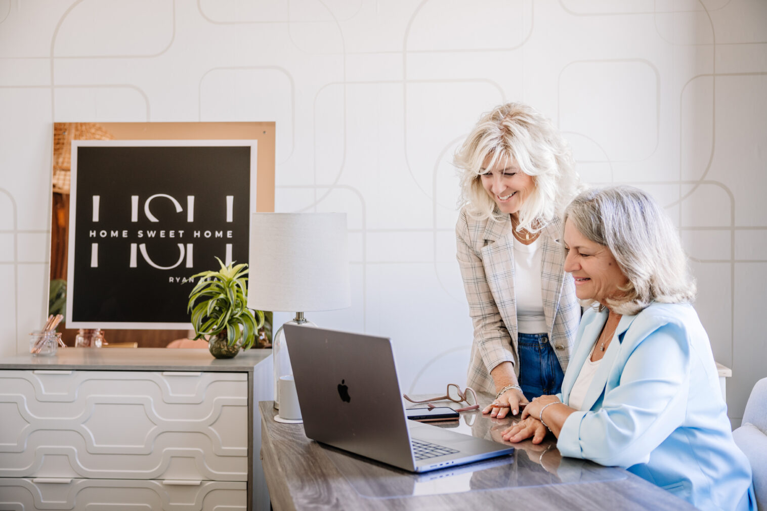 two realtors look at a laptop with their sign in the background