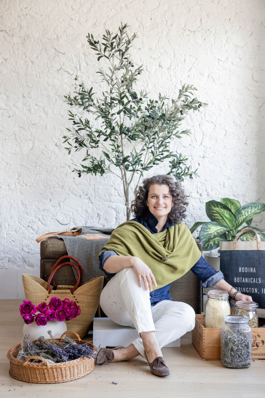 Woman in a green wrap sits on the ground with flowers and herbs beside her