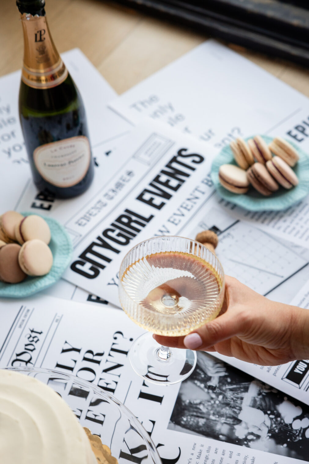 close up of a woman's hand holding a glass of champage in front of newspaper headlines that read "citygirl events"