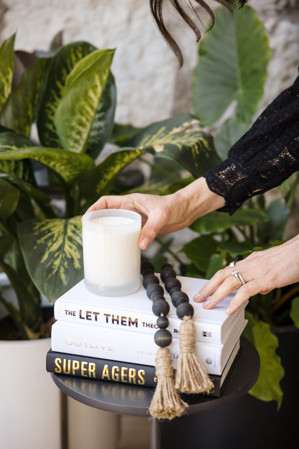 a woman's hands place a candle on top of a stack of self-help books