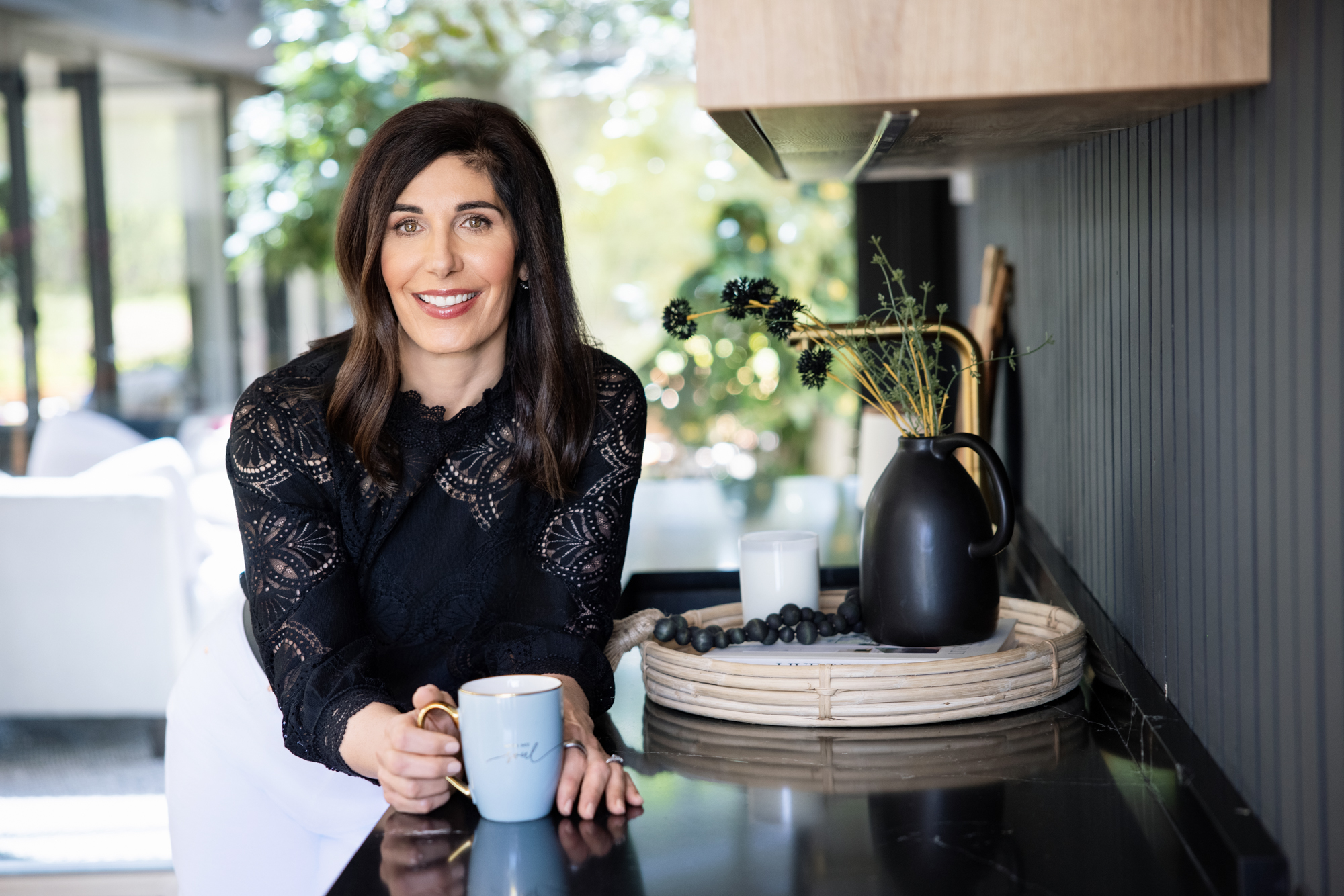 woman leans on a kitchen counter holding a mub