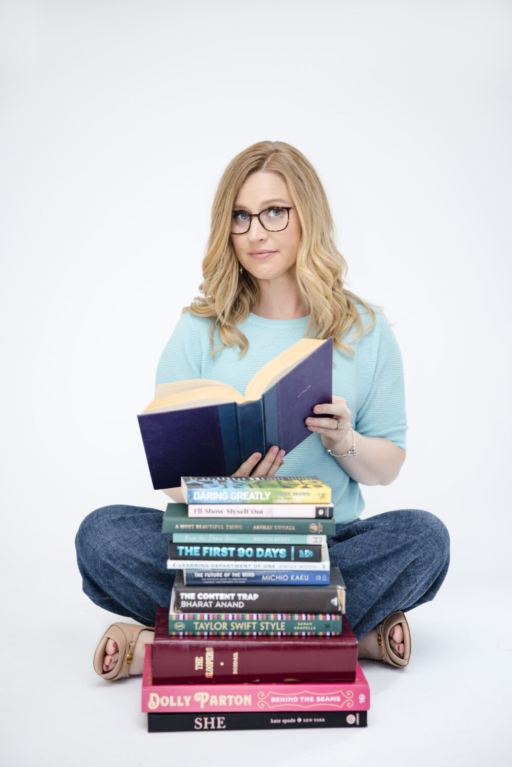Woman holding a book behind a pile of books, looking playfully skeptical at the camera in a Chicago brand photography session.