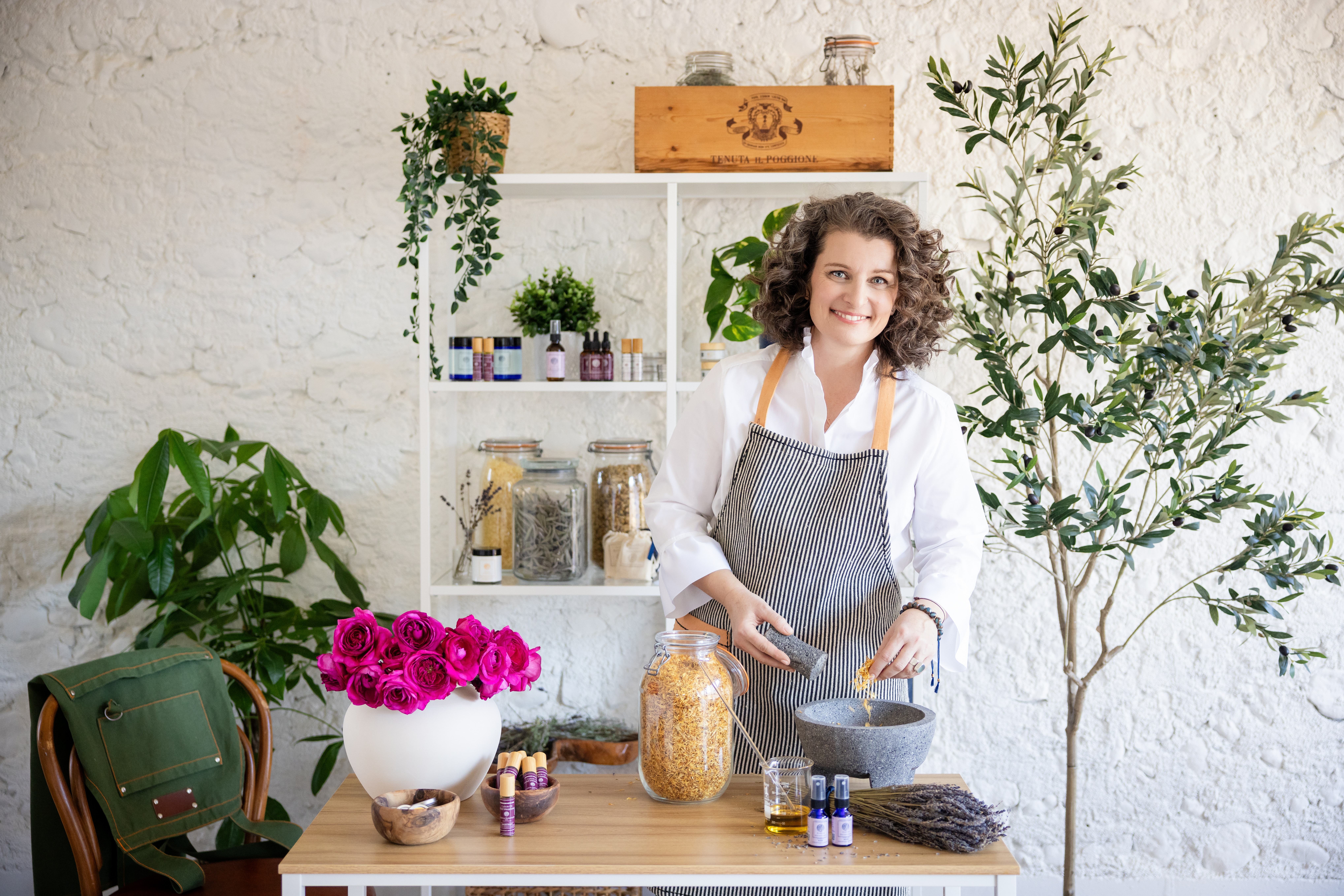 Woman in apron surrounded by herbs, smiling while grinding herbs in a mortar and pestle during a Chicago brand photography session.